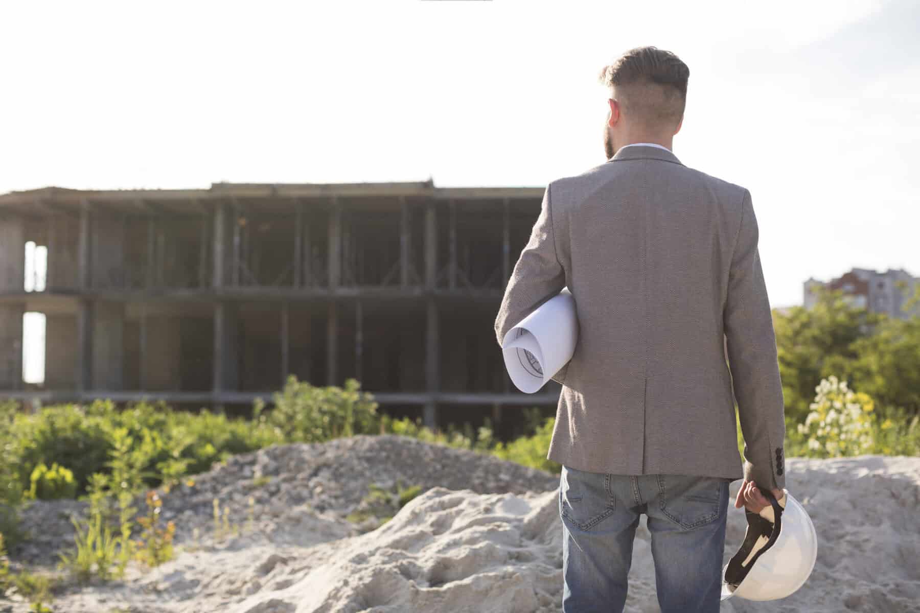 Relazioni specialistiche relative ai temi CAM e DNSH 2 rear view male architecture holding blueprint hard hat looking construction site scaled